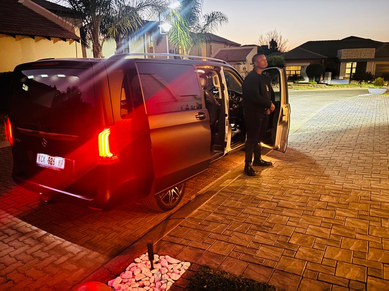 KM VIP officer standing guard beside executive Mercedes V-Class vehicle at night